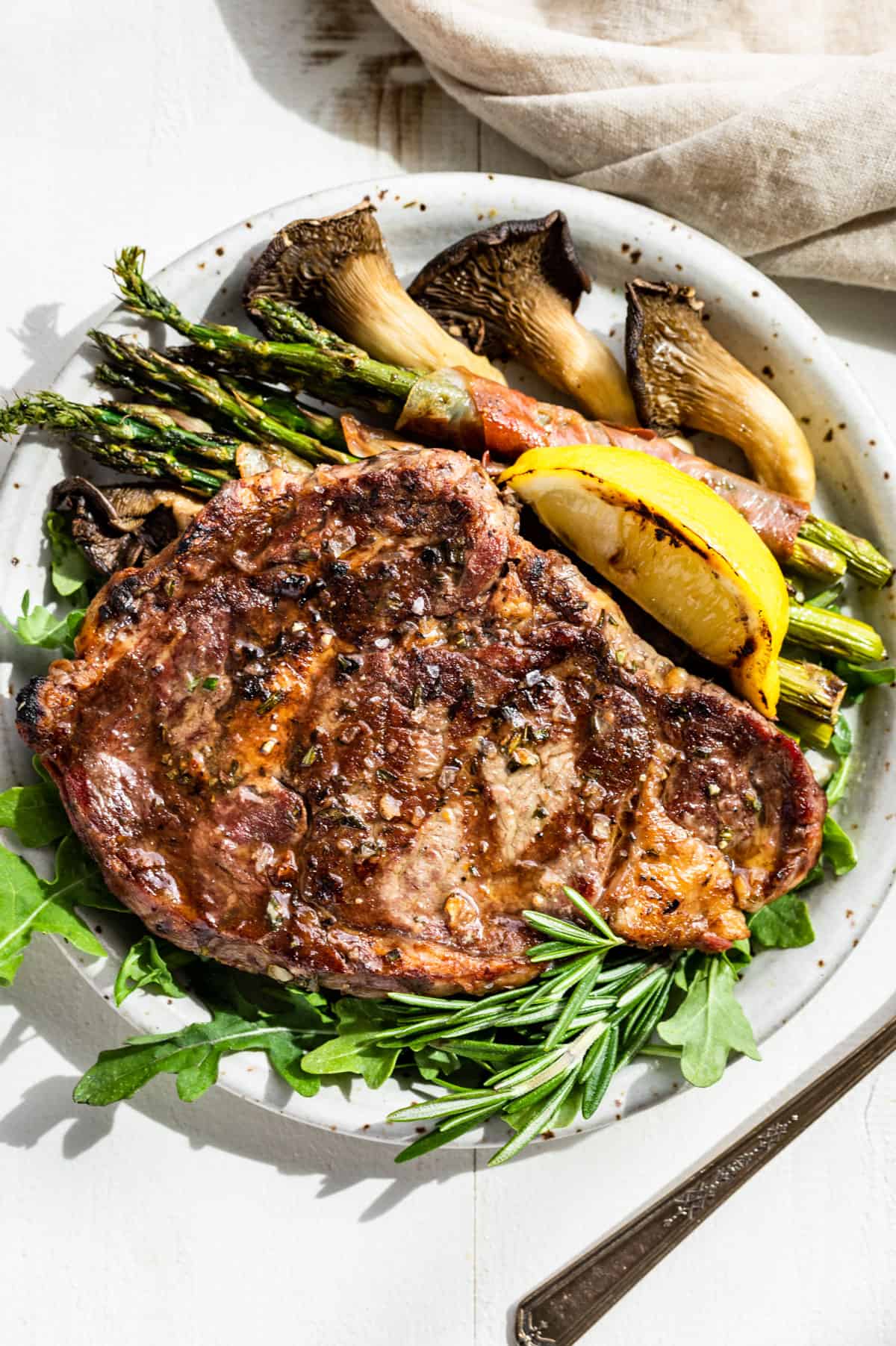 Closer macro view Looking down at the finished Tuscan Steak on a bed of arugula with a lemon wedge, asparagus, and mushrooms on the side.