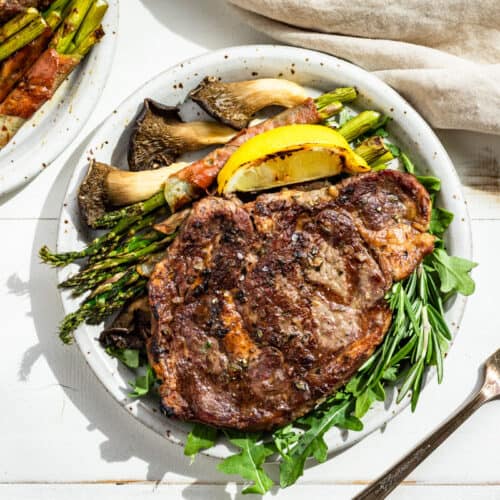 Looking down at the finished Tuscan Steak on a bed of arugula with a lemon wedge, asparagus, and mushrooms on the side.