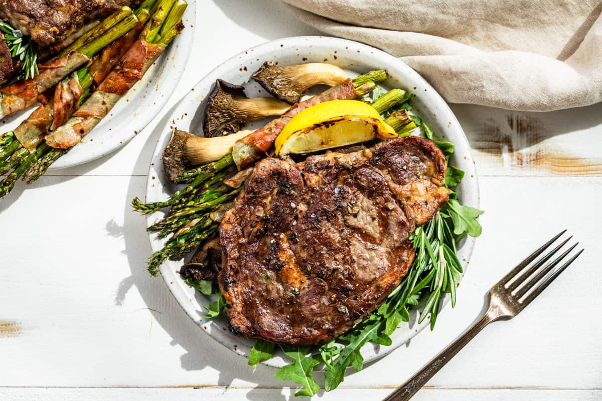 Looking down at the finished Tuscan Steak on a bed of arugula with a lemon wedge, asparagus, and mushrooms on the side.