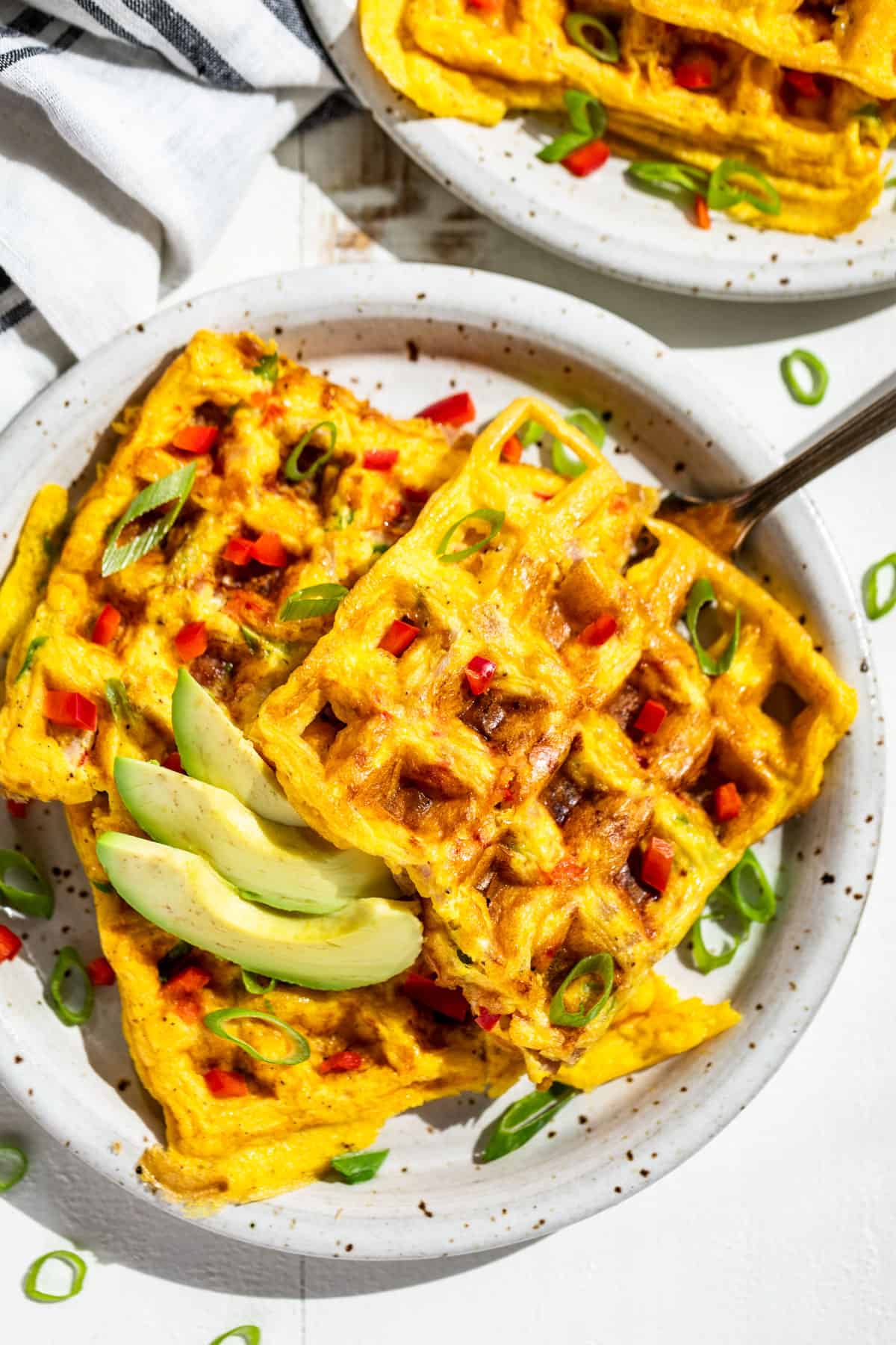 Straight down view of Western Omelet Waffles on two speckled plates topped with sliced green onion and avocado.