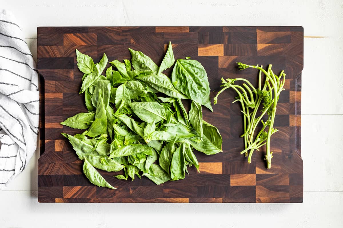 Basil leaves removed from the stems on a wooden cutting board.