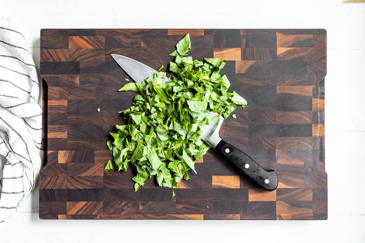 Roughly chopped basil on a wood cutting board with a chef's knife on the side.