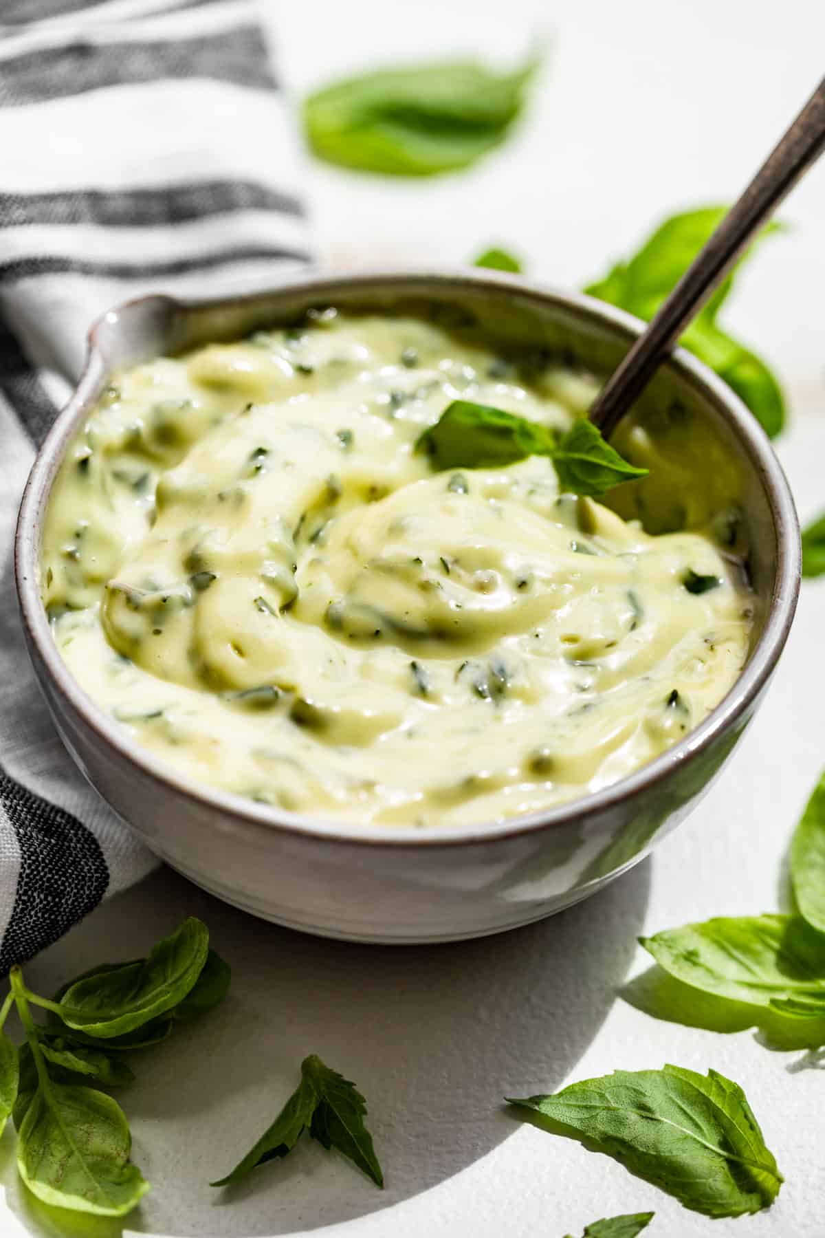 A small pottery bowl filled with Basil Aioli with basil leaves around it.