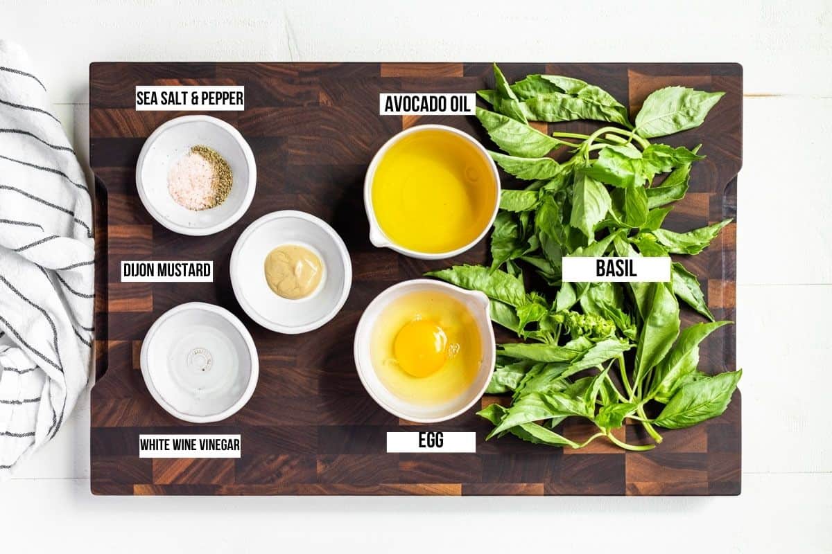 Ingredients for Basil Aioli, basil leaves, oil, egg, sea salt, pepper, and vinegar in small bowls on a wooden cutting board.