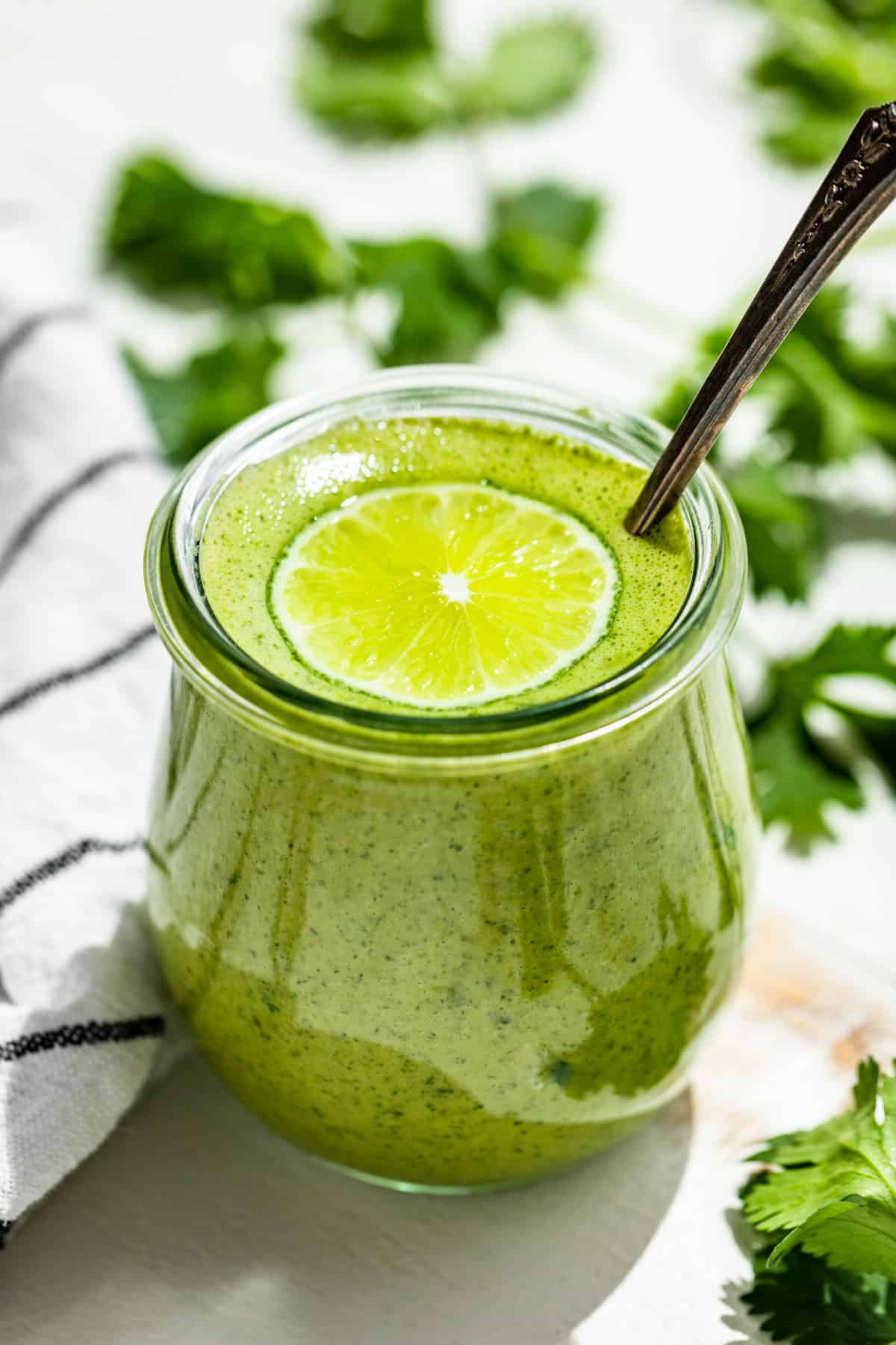 Cilantro Lime Dressing in a glass jar topped with a slice of lime and cilantro sprigs around it.