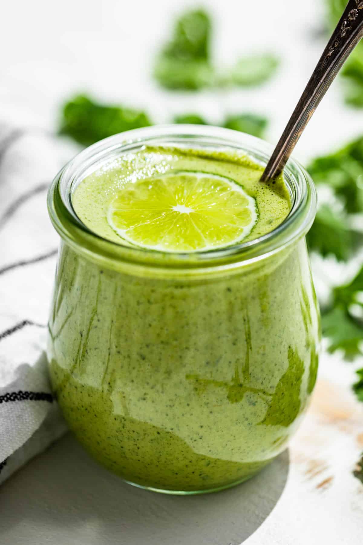 Side view of Cilantro Lime Dressing in a glass jar on a white background.