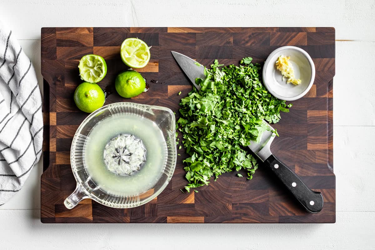 Juiced limes, chopped cilantro, and minced garlic on a wood cutting board.