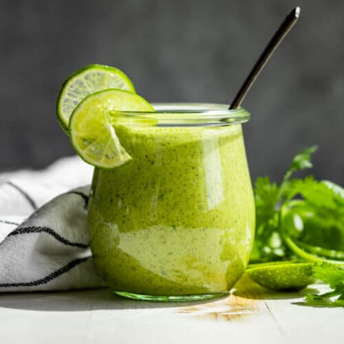 Cilantro Lime Dressing in a glass jar with a silver spoon in it and topped lime slices.