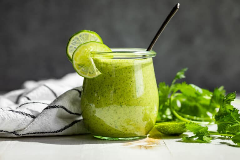 Cilantro Lime Dressing in a glass jar with a silver spoon in it and topped lime slices.
