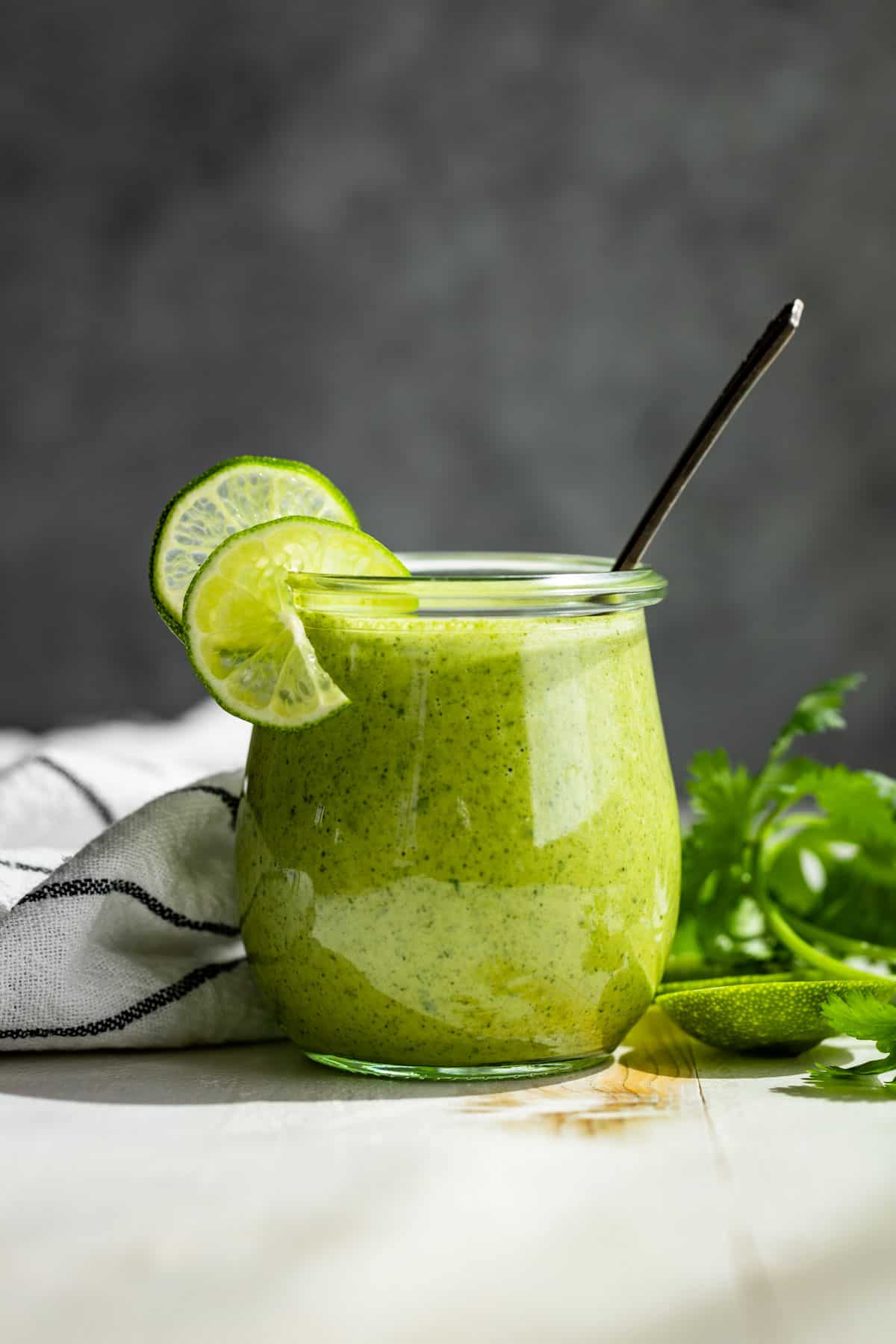 Cilantro Lime Dressing in a small glass jar with lime slices on the side and a silver spoon.