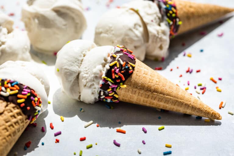 Side view of three chocolate dipped ice cream cones with Coconut Ice Cream and sprinkles.