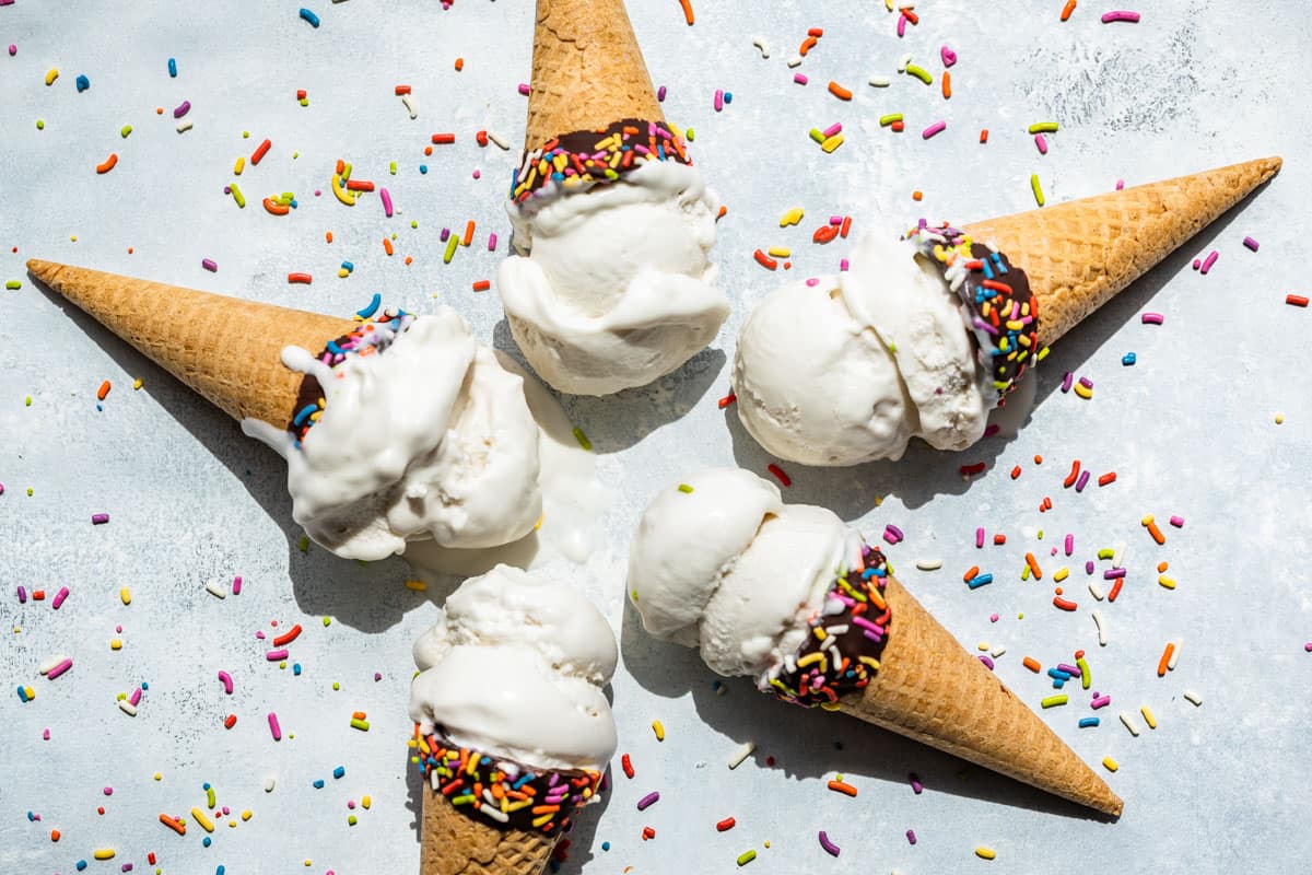 Five ice cream cones filled with scoops of Coconut Ice Cream with sprinkles around them.