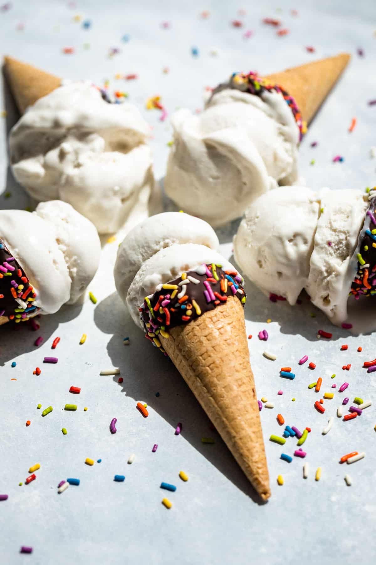 Five chocolate dipped ice cream cones filled with Coconut Ice Cream with sprinkles around them.