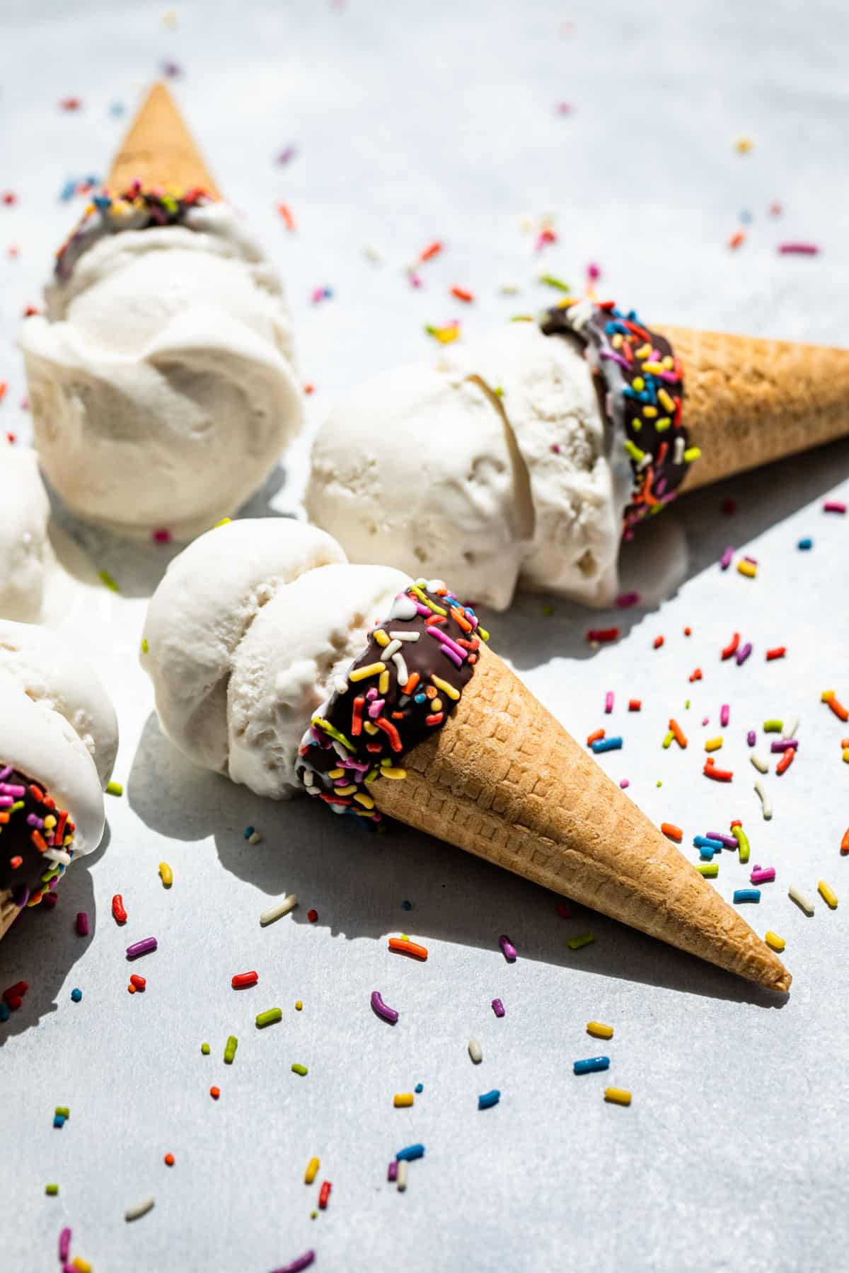 Side view of Coconut Ice Cream scooped into chocolate dipped cones with sprinkles.