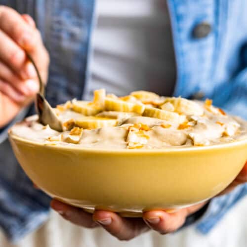 A yellow bowl filled with Coconut Banana Nice Cream with a person in a blue jacket scooping some out.