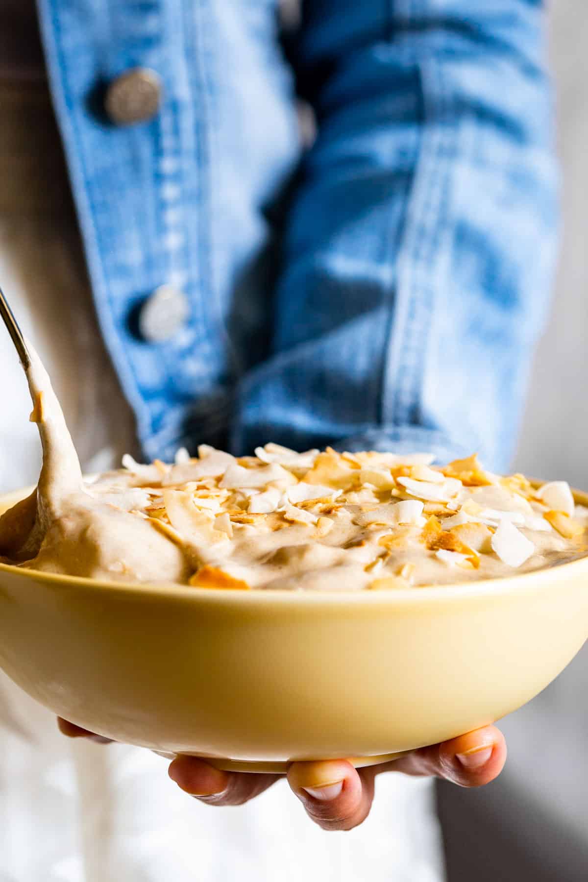 A close view of the Coconut Banana Nice Cream topped with toasted coconut with a gold spoon scooping some out.
