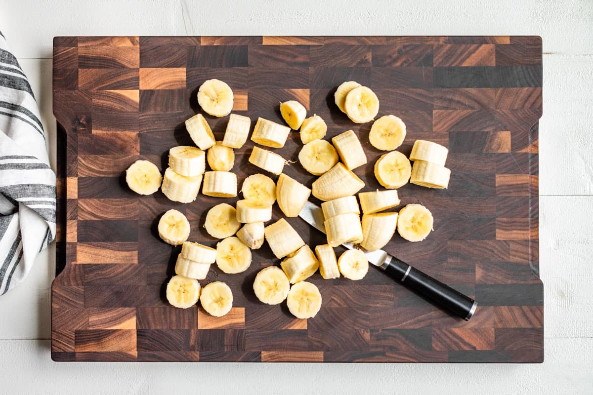 Sliced bananas on a wood cutting board with a pairing knife.