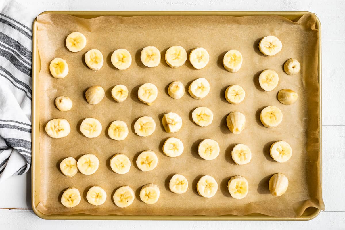 Sliced bananas on a parchment lined baking sheet ready for freezing.