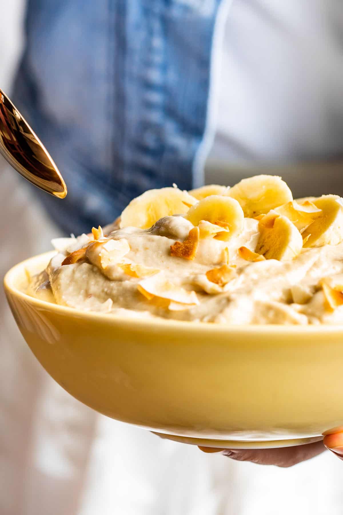 Close view of a yellow bowl filled with Creamy Coconut Banana Nice Cream with a gold spoon dipping in.