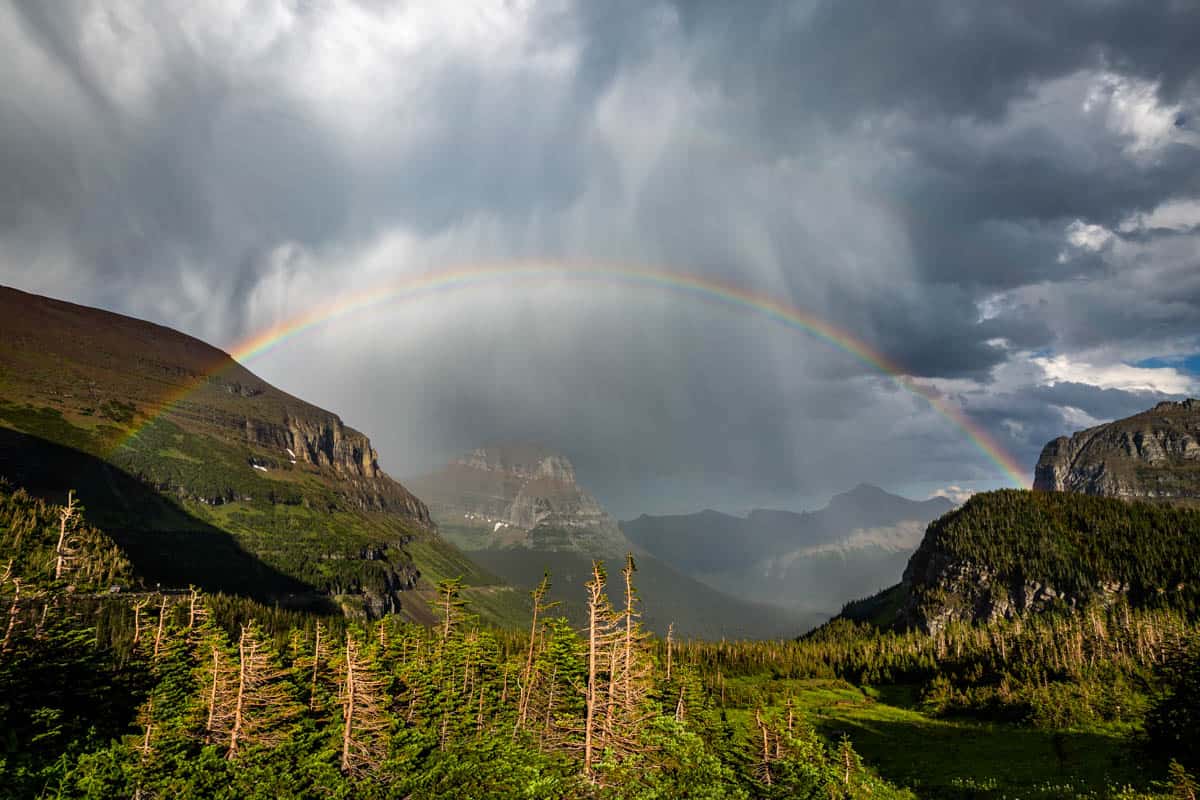 View of Going to the Sun mountain with a rainbow over the top and dark and stormy skies.