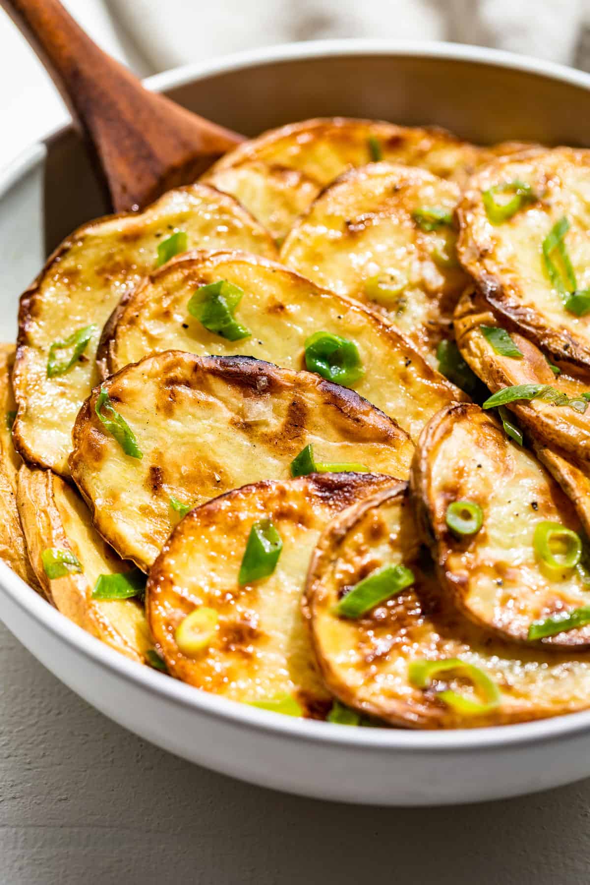 A large white bowl filled with grilled sliced potatoes and topped with green onions.