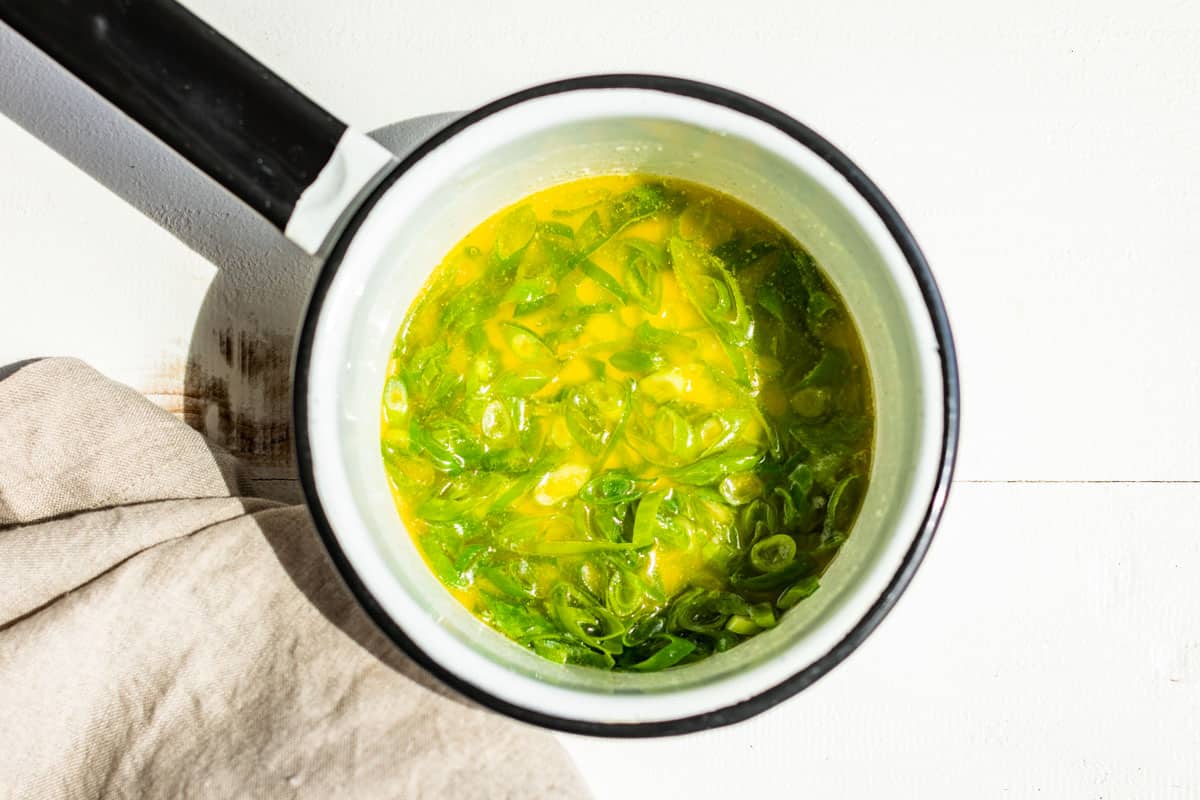 A small white enamel pot with melted butter and green onions.