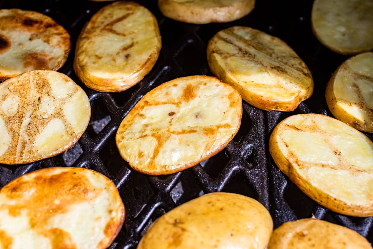 Turned potato slices on the grill with grill marks on top.