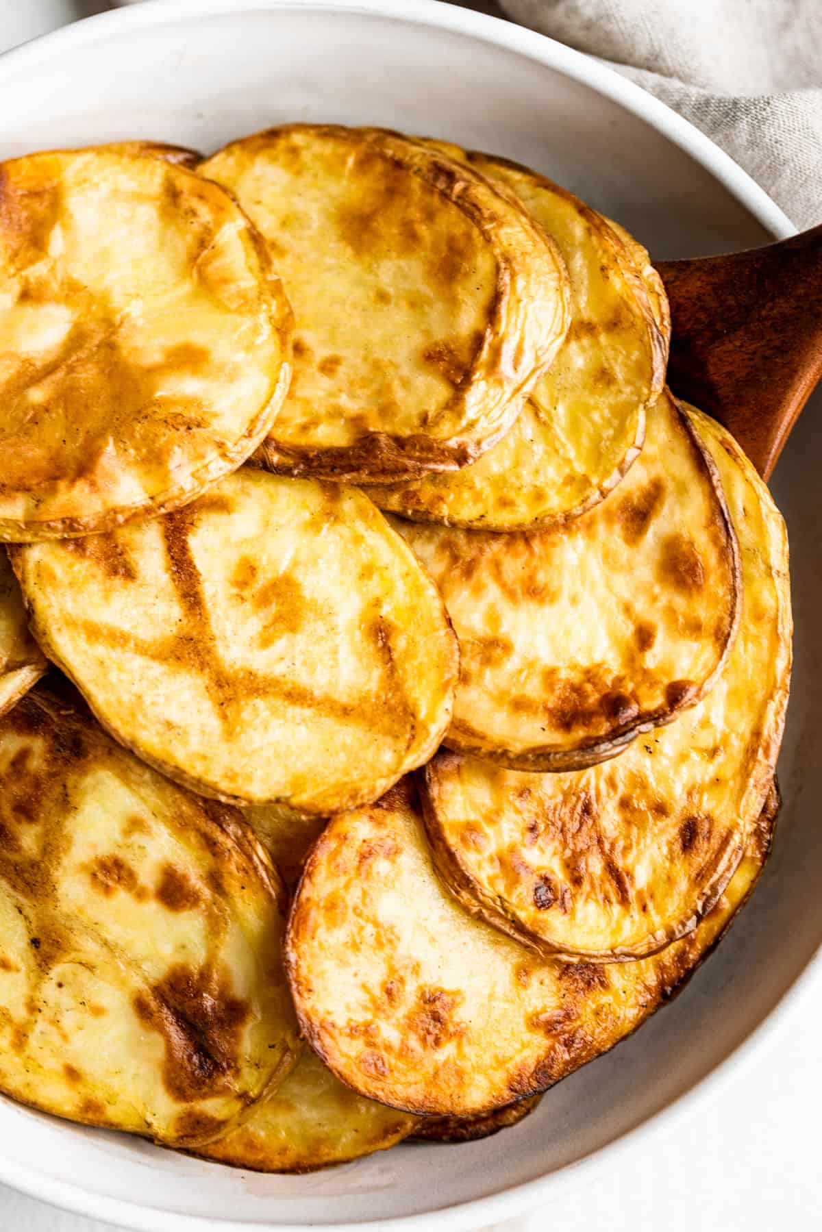 Plain grilled sliced potatoes in a white bowl with a wooden spoon.