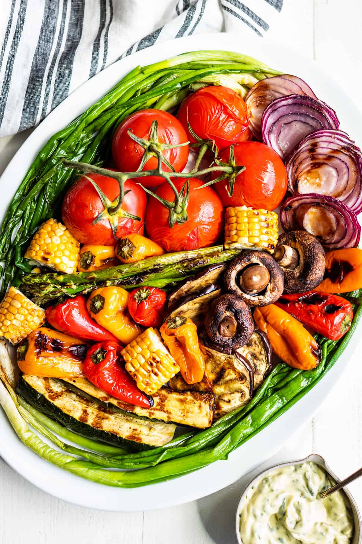 All the grilled veggies piled onto a large white platter with basil aioli in a small bowl on the side.