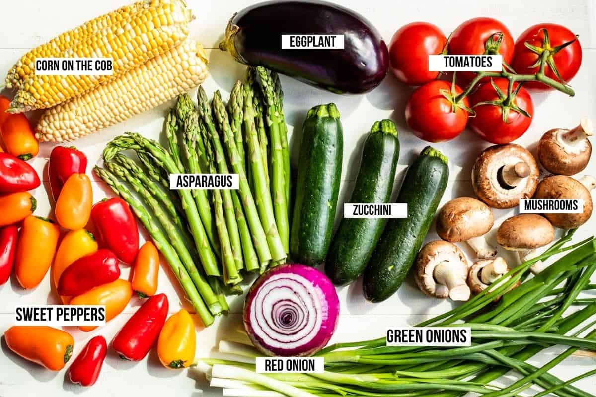 Prepped veggies for grilling, corn on the cob, peppers, asparagus, a red onion, zucchini, green onions, eggplant, tomatoes, and mushrooms.