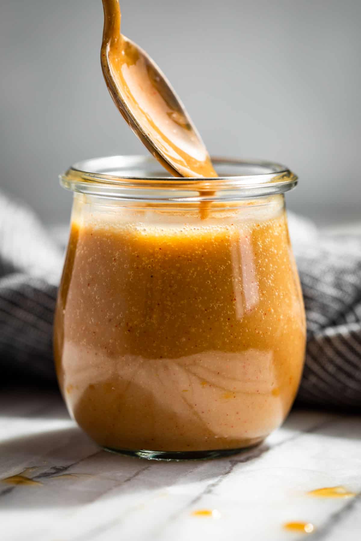 Honey Mustard Sauce in a glass jar with a sliver spoon scooping some out.