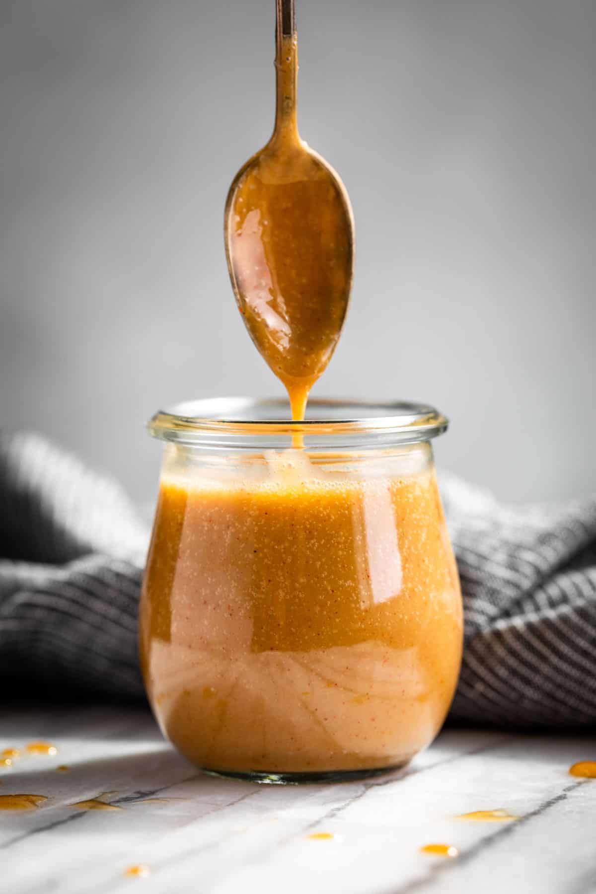 Honey Mustard Sauce in a glass jar with a sliver spoon being lifted out and sauce dripping down.