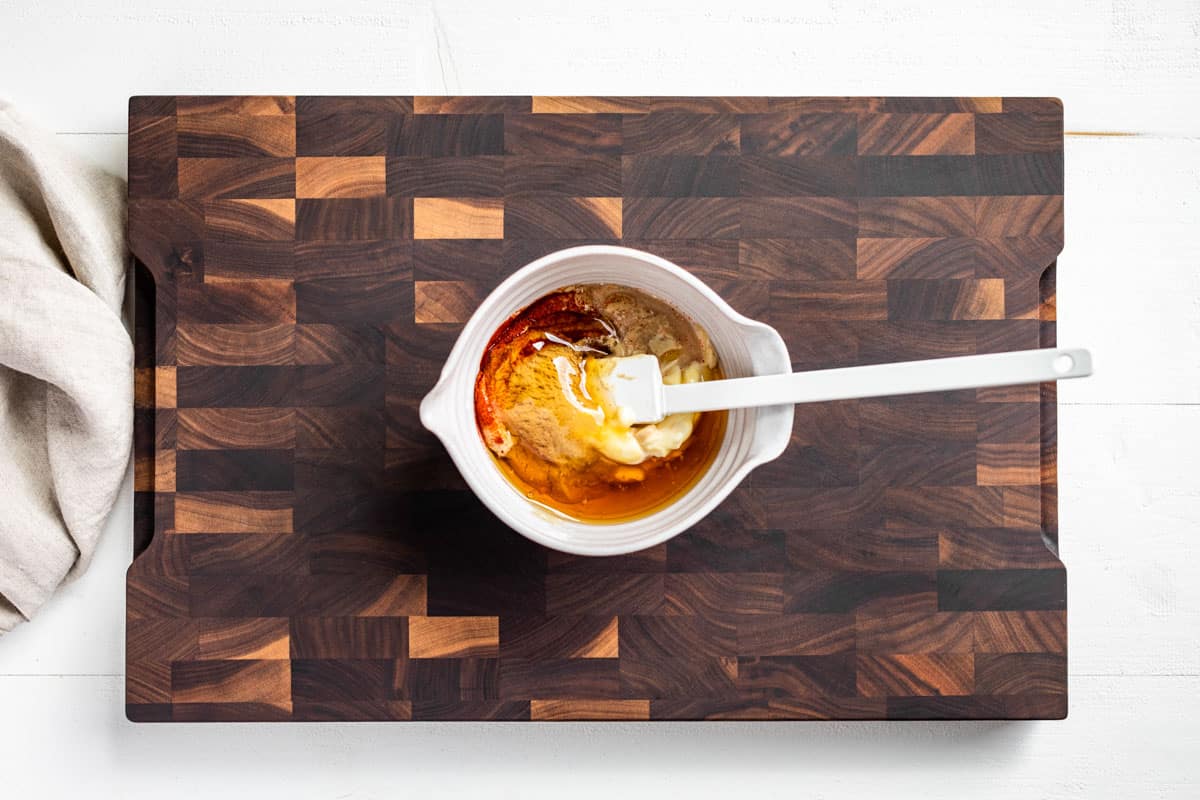 Adding the ingredients for the Honey Mustard Sauce to a small mixing bowl on a wood cutting board.