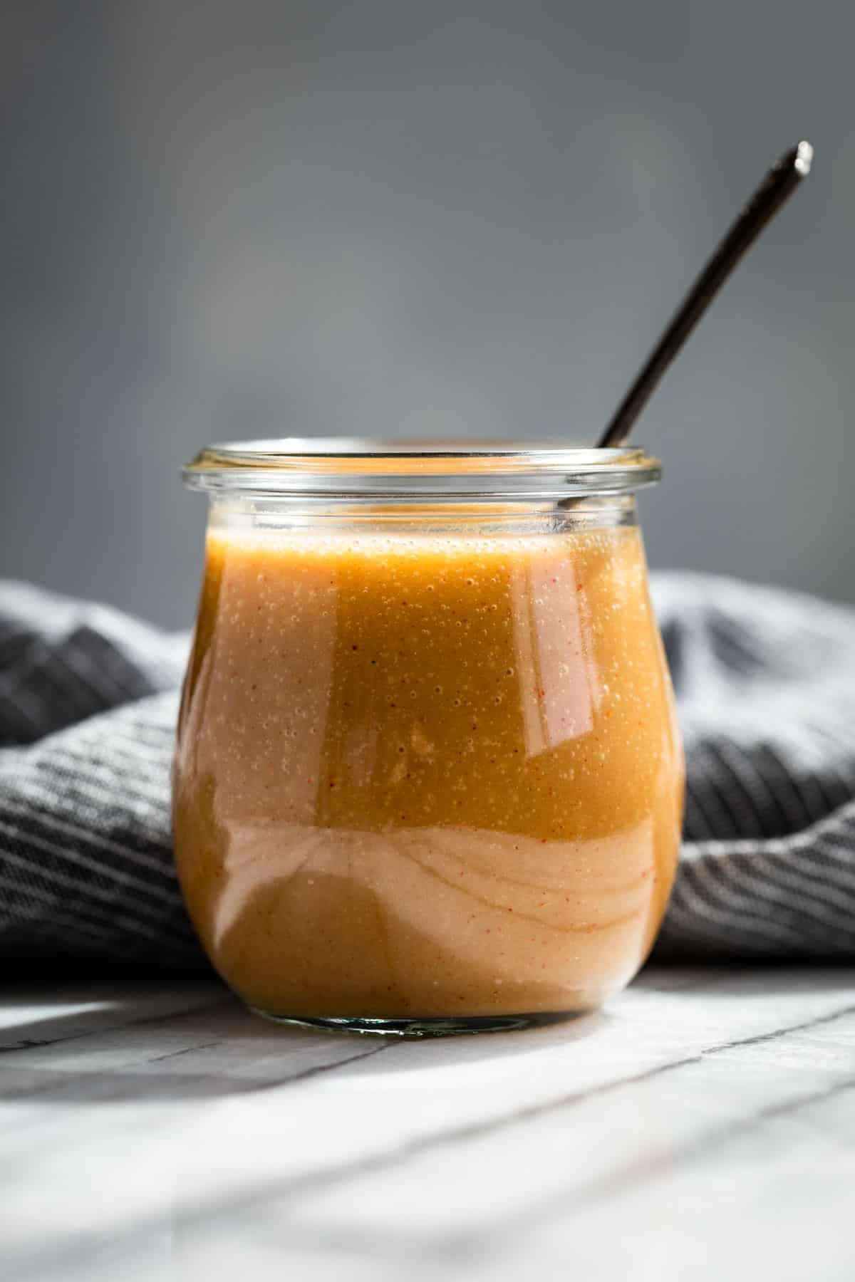 Honey Mustard Sauce in a glass jar with a silver spoon in it.