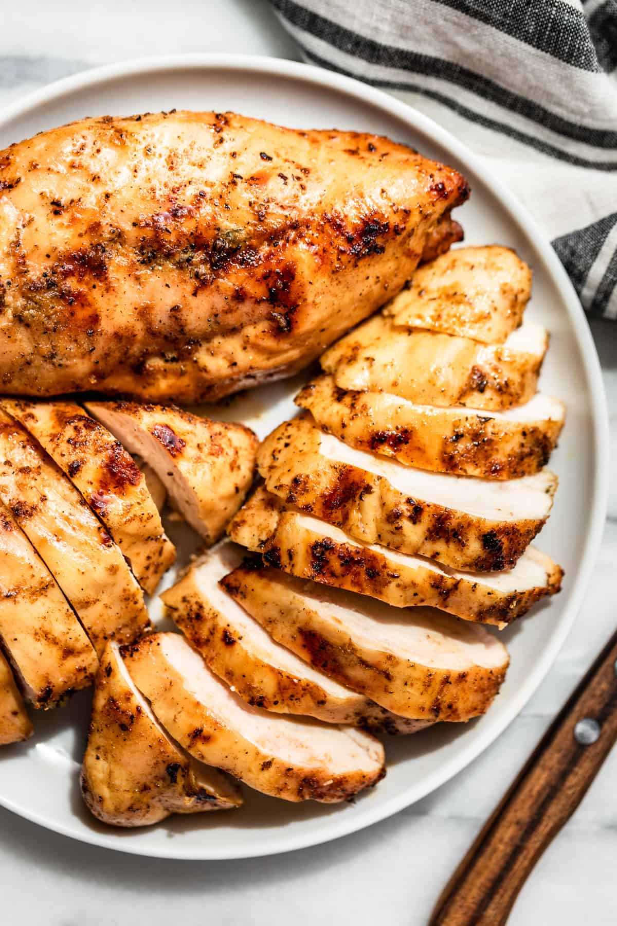 Sliced Smoked Chicken Breasts on a white plate with a wood handled knife on the side.