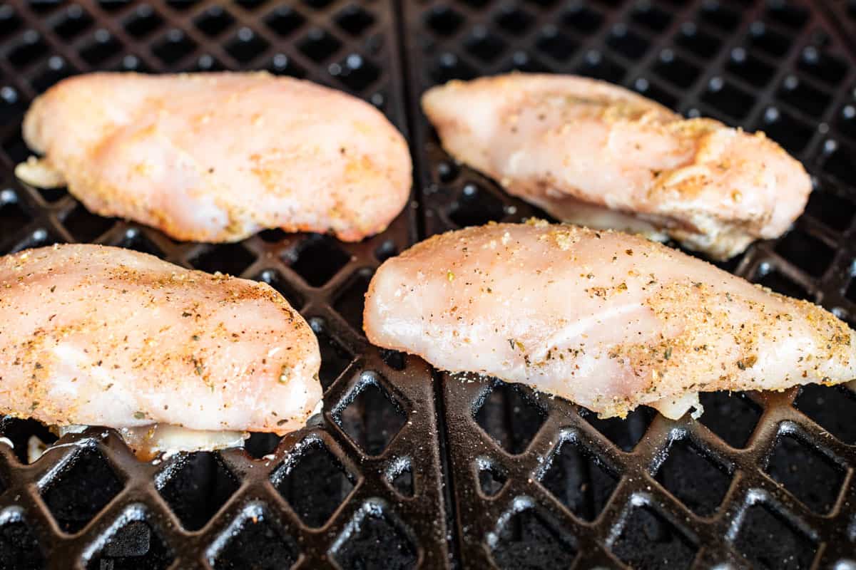 Seasoned chicken breasts on the grill being smoked.