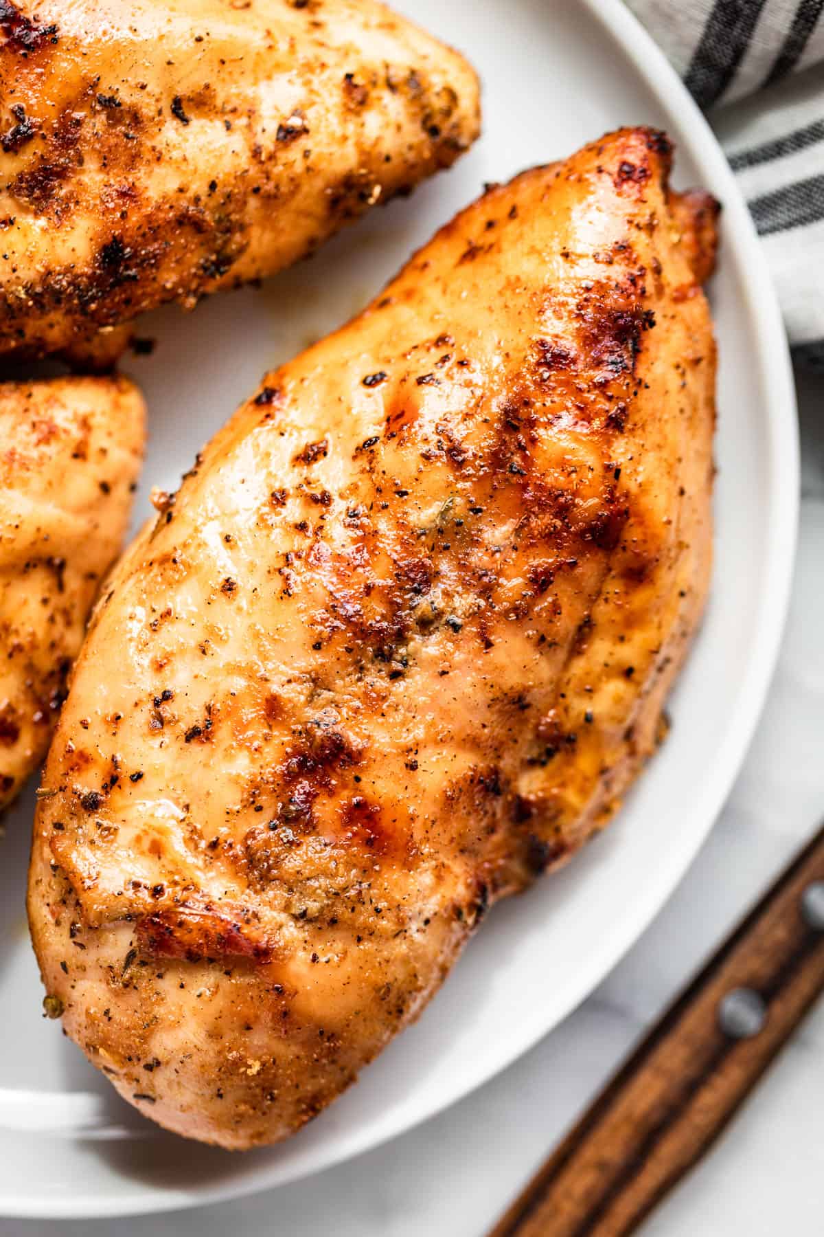 A whole Smoked Chicken Breast on a white plate with a wood handled knife on the side.