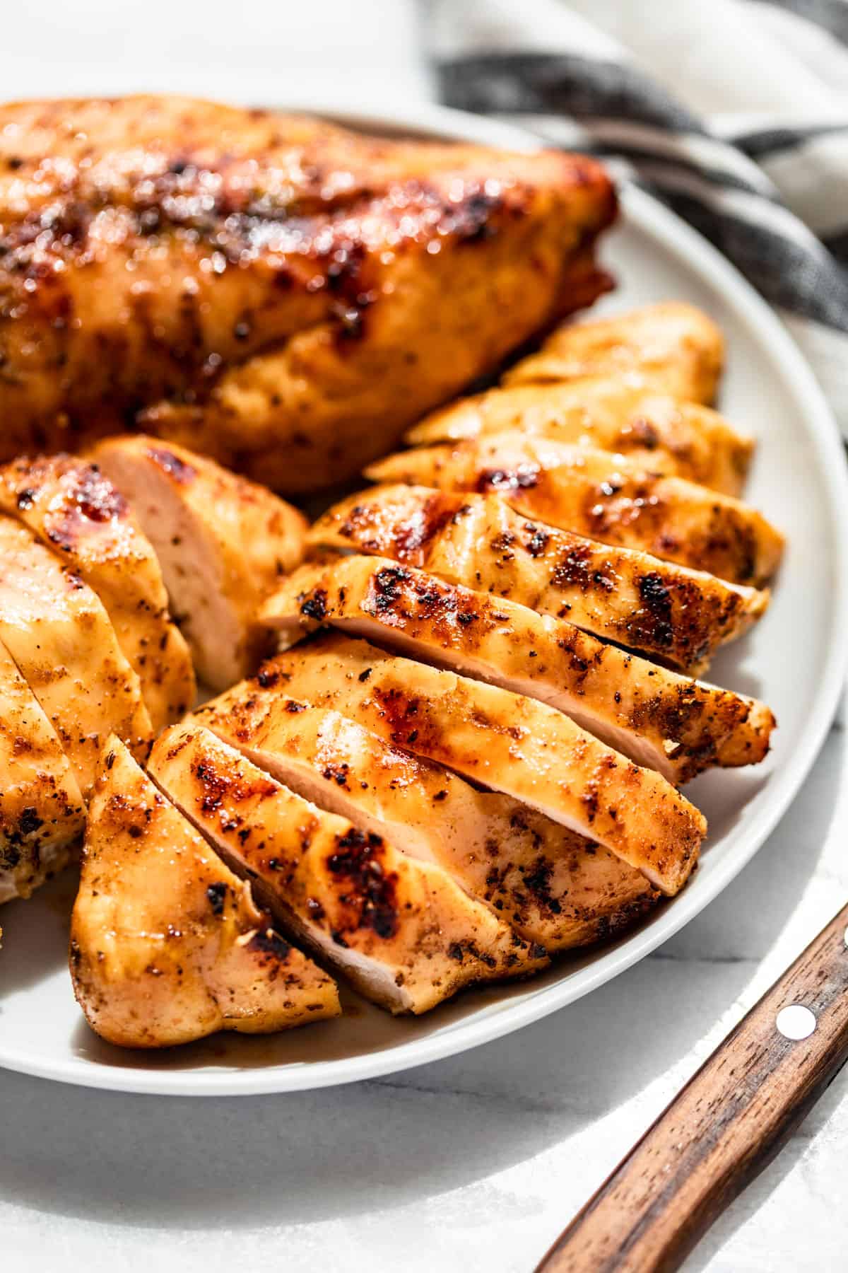 Close side view of sliced Smoked Chicken Breasts on a white plate with a blue and white striped linen in the background.