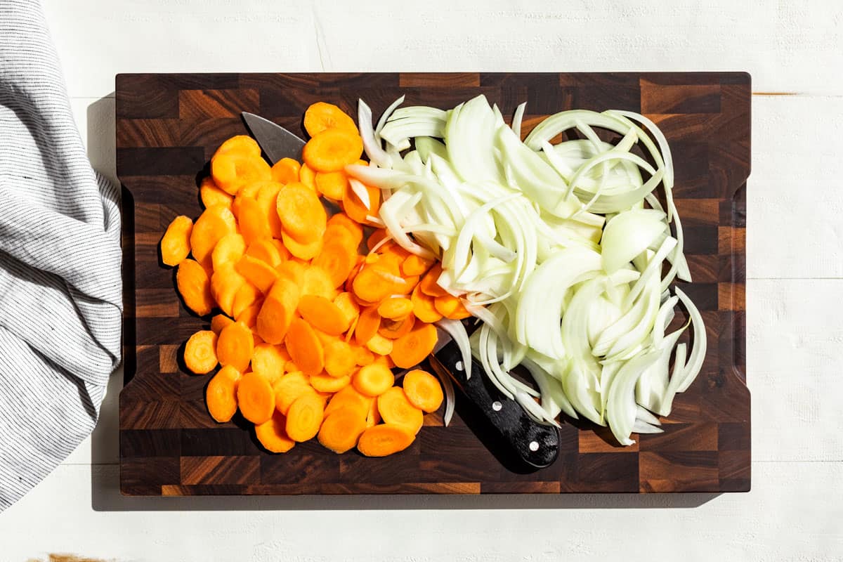 Sliced carrots and onions on a wood cutting board.