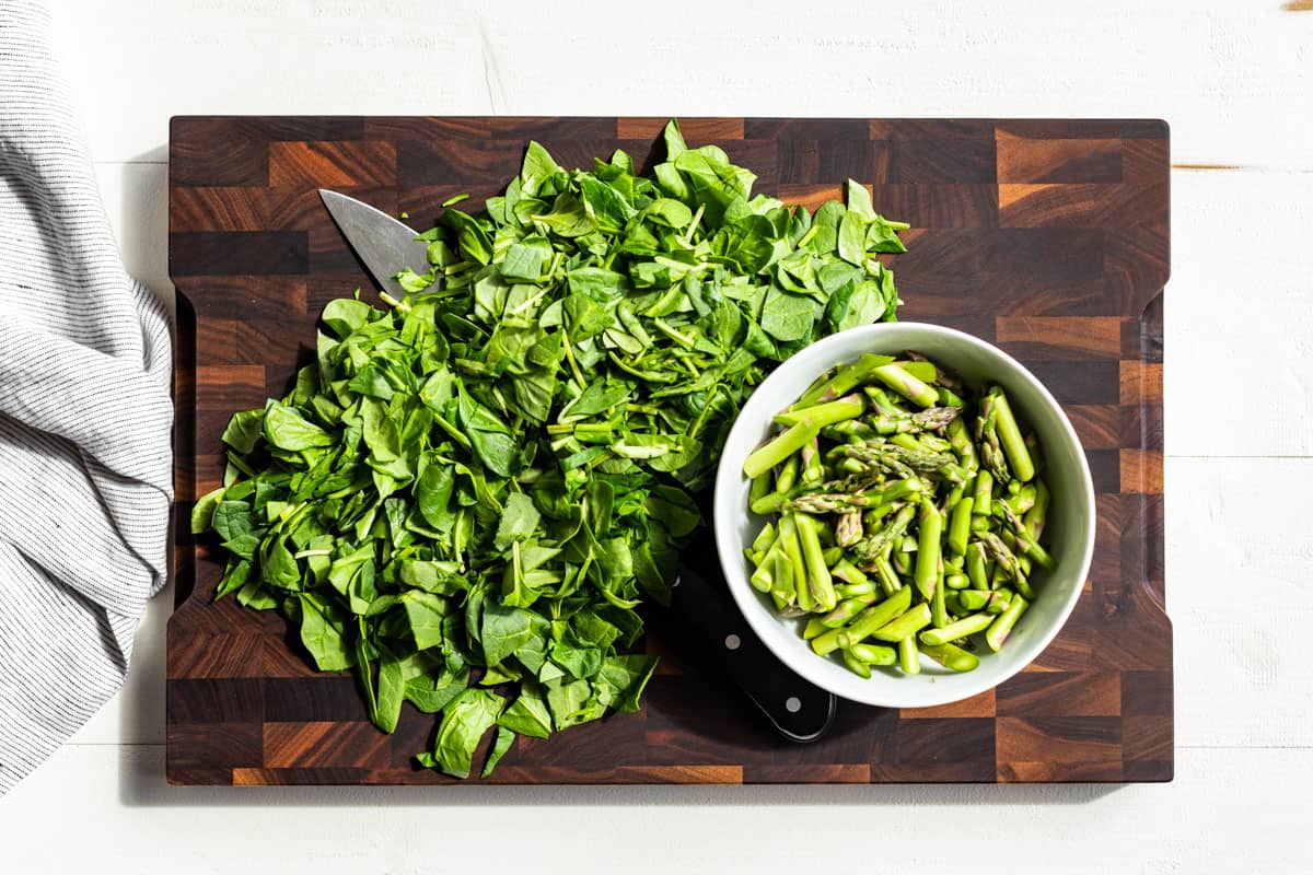 Chopped spinach and sliced asparagus on a wood cutting board.