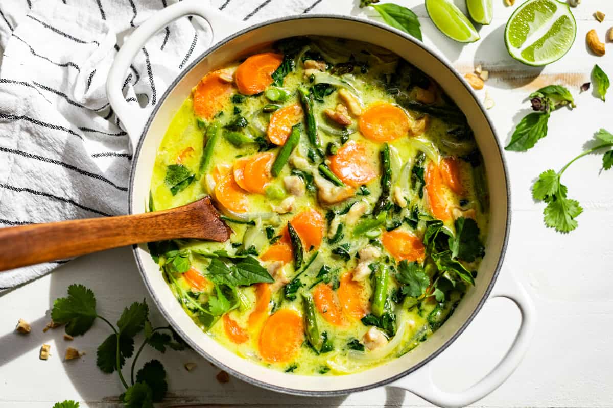 Straight down view of Thai Green Curry with a wooden ladle with lime wedges and cilantro sprigs on the side.