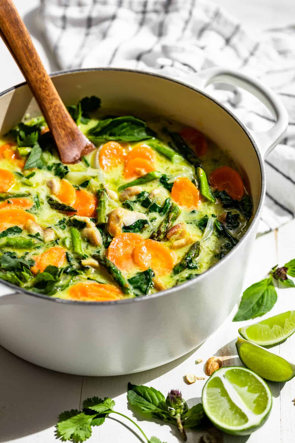 Side view of Thai Green Curry in a large white pot with a wooden ladle.