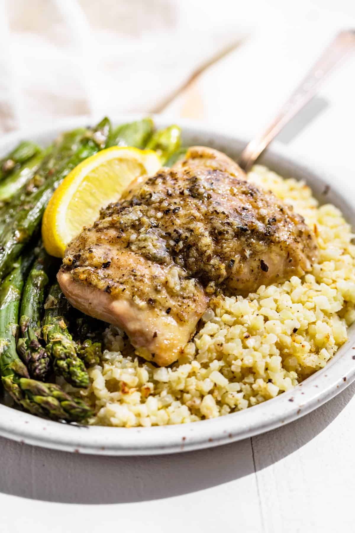 Garlic Herb Chicken and Asparagus on a pottery plate with a lemon wedge on top.