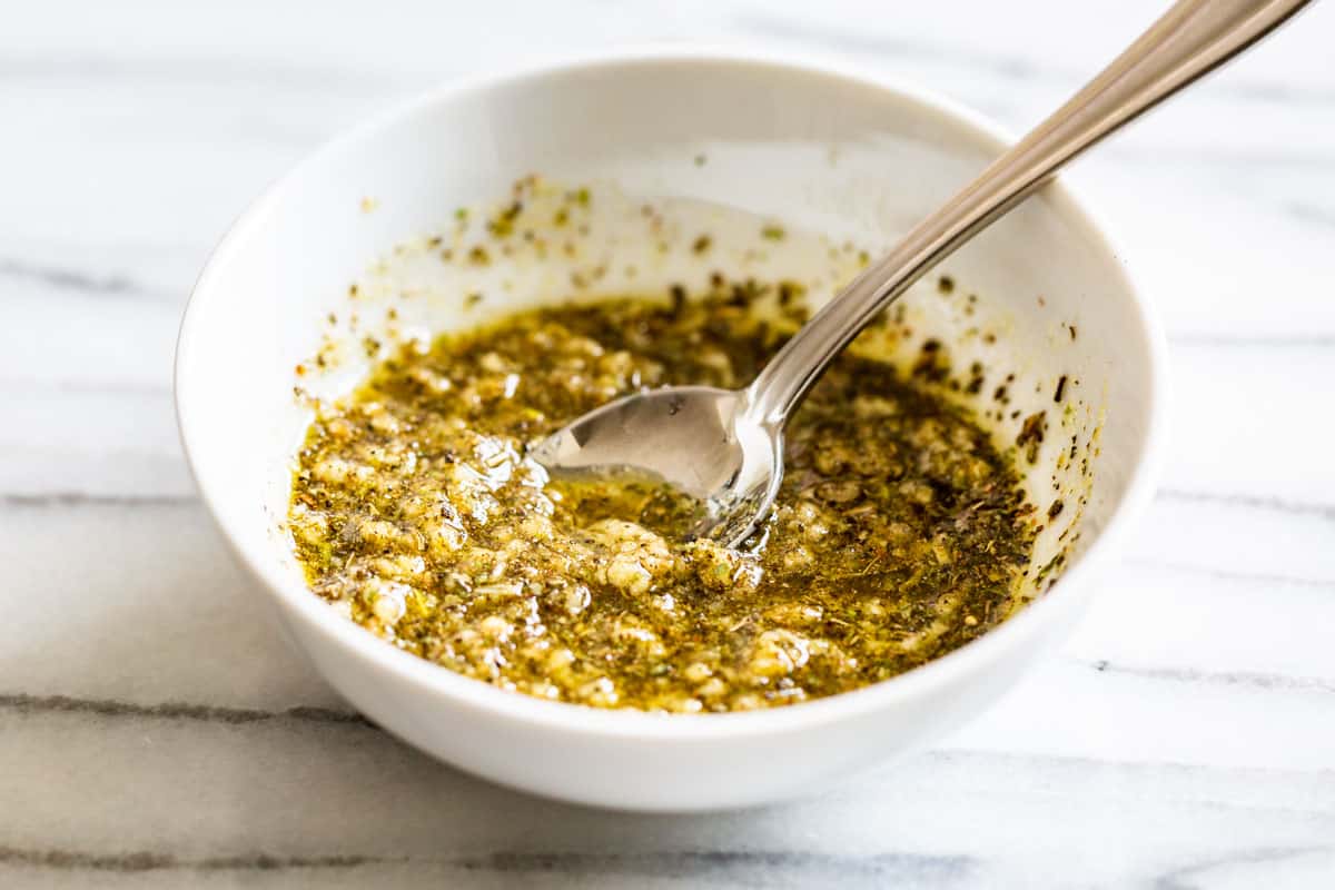 Garlic herb olive oil mixture in a white bowl.