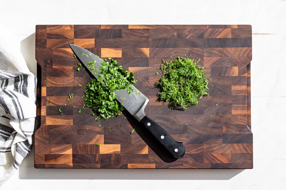 Roughly chopped parsley and dill on a wood cutting board.