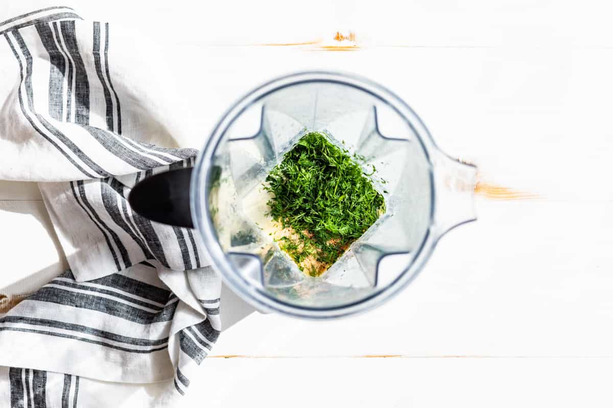 Adding the chopped parsley and dill to the ranch dressing base in a blender container.