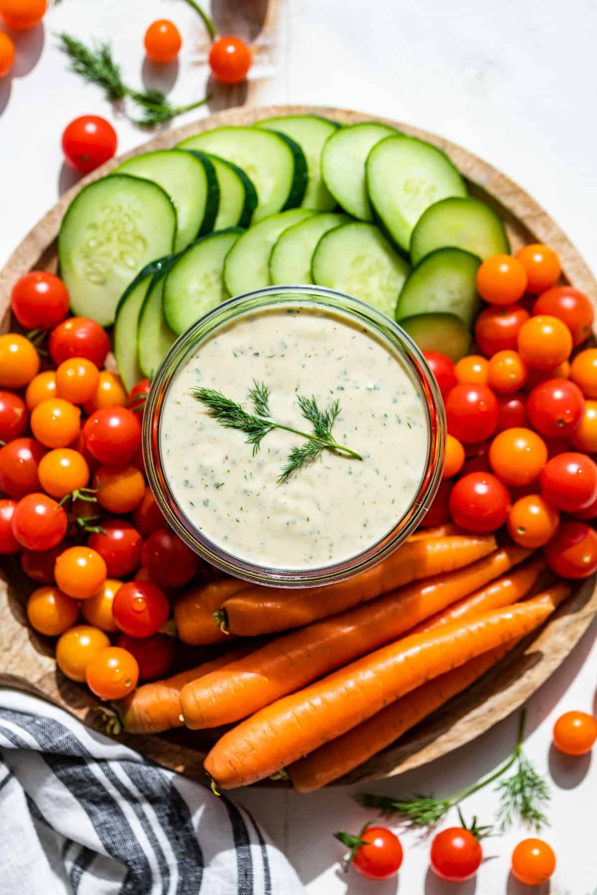 A round wood platter filled with veggies with ranch dressing in a container in the center.