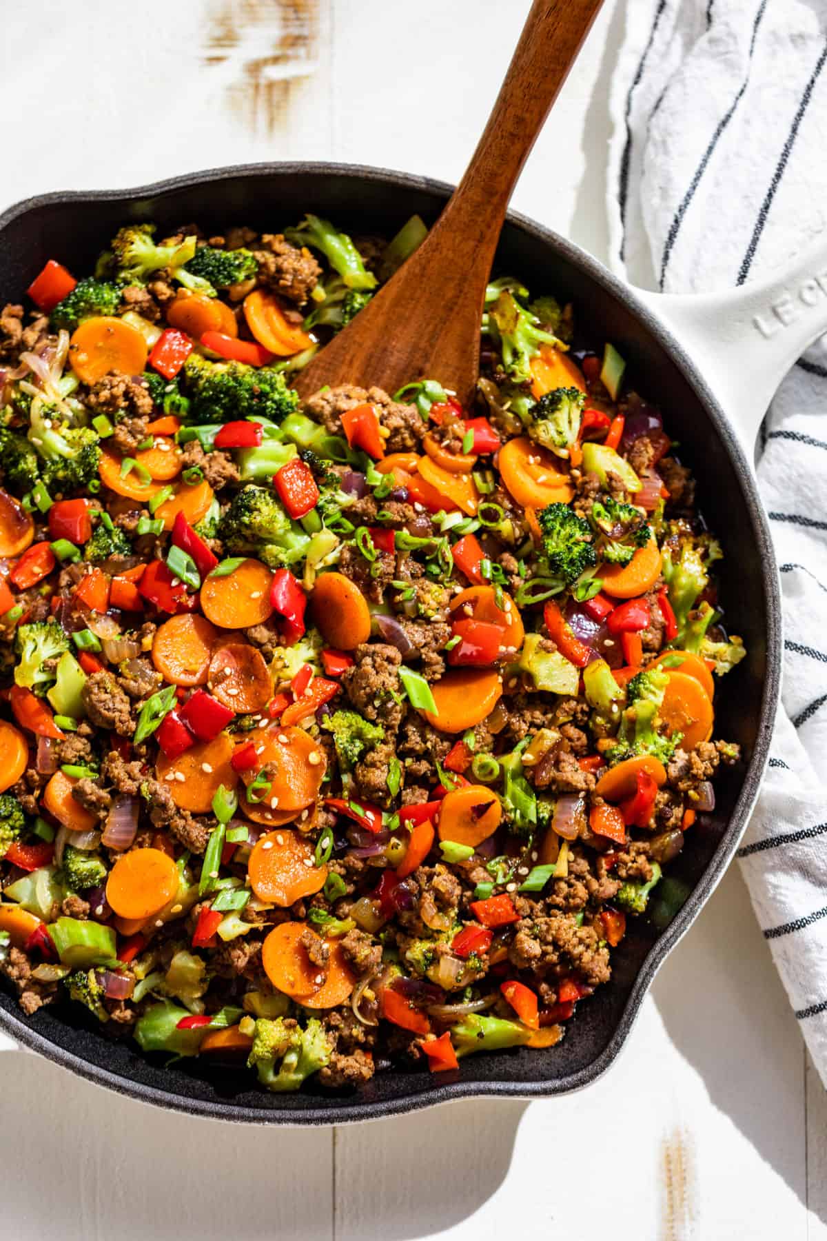 A large white skillet filled with Ground Beef Stir Fry with a wooden spatula scooping some out.