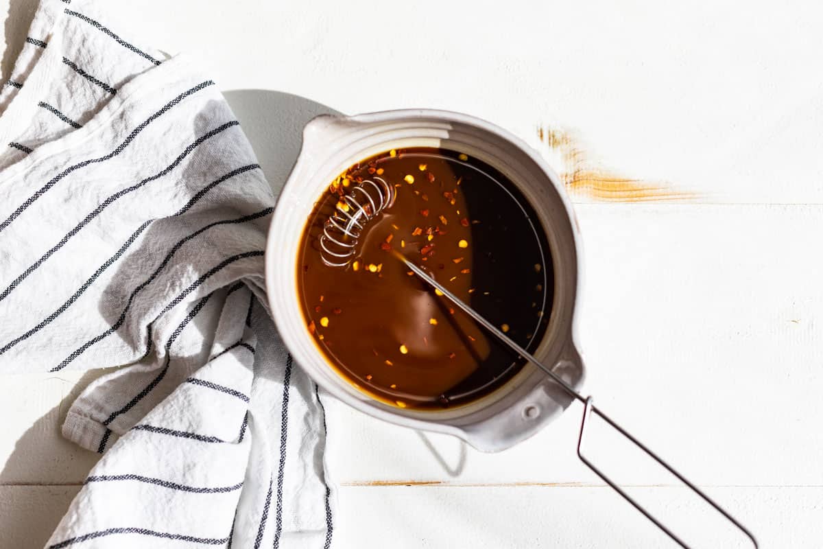 Stir Fry Sauce being whisked together in a small pottery bowl on a white background.