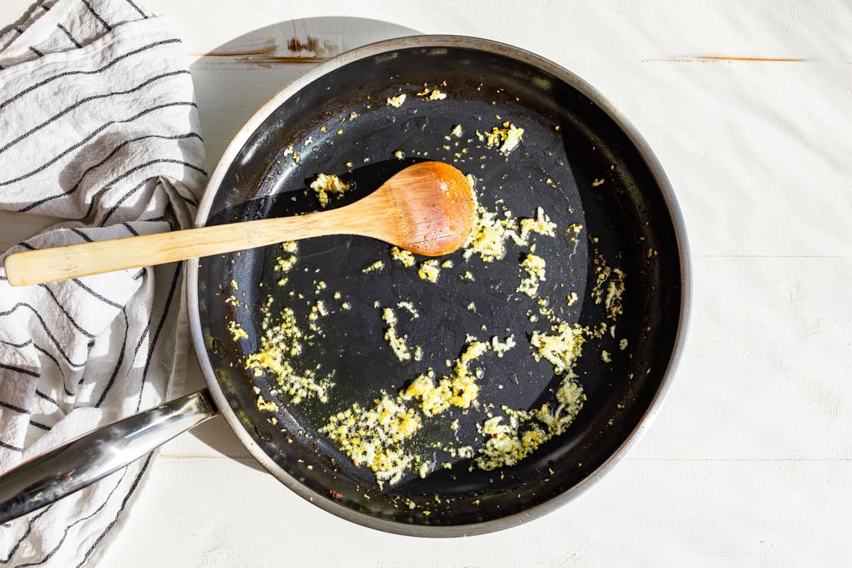 Minced garlic and ginger being sautéed in a large skillet.